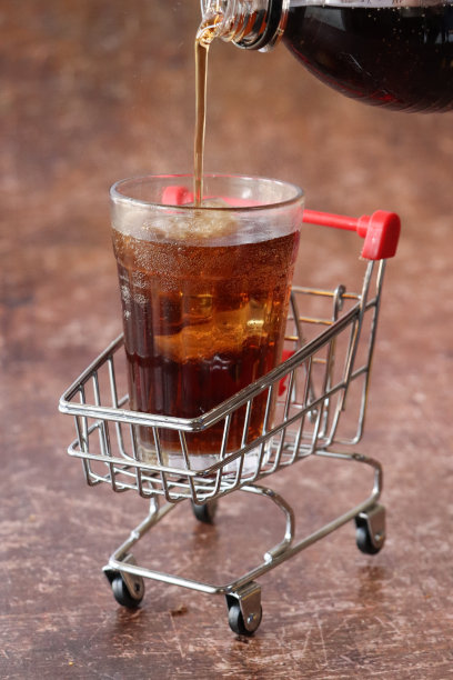 汽水从塑料汽水瓶倒进个人的特写图像，迷你冰块餐杯，模型购物车，碳酸饮料，棕色背景，前景的焦点，不健康的饮食观念图片下载