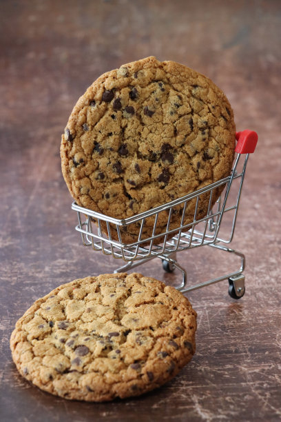 两个牛奶巧克力饼干的特写图像，一个饼干的微缩，模型购物车，不健康的食品零食，棕色背景，重点在前景图片下载