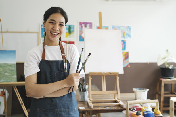 年轻的亚洲女艺术家在艺术工作室看着相机，微笑着。图片下载