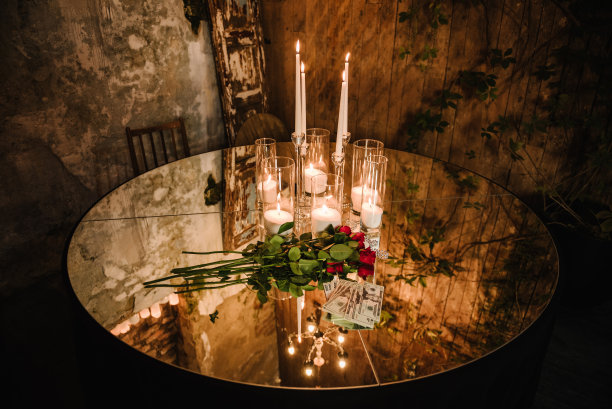 聚会用的镜子桌。别致的桌子上装饰着蜡烛、鲜花和婚礼请柬的钱。豪华的乡村风格的桌子背景傍晚照明灯泡在餐厅举办晚宴图片下载