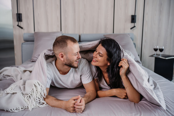 爱的夫妇在床单下分享温柔的凝视，创造温暖和感情的氛围，以别致的卧室为背景图片下载