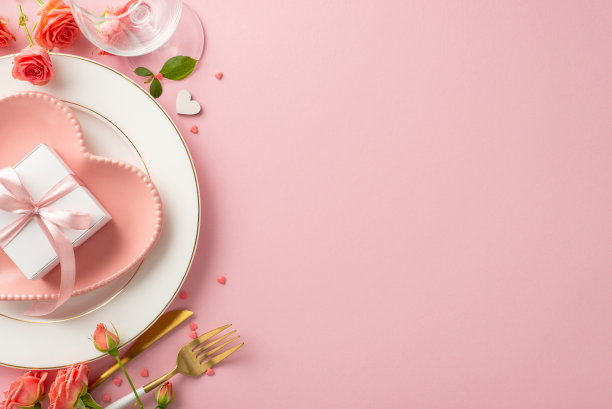 亲密晚餐约会:浪漫的餐桌设置的俯视图照片，以心形的盘子，餐具，酒杯，玫瑰和粉红色的背景礼物盒为特色。为文字或广告留出足够的空间图片下载