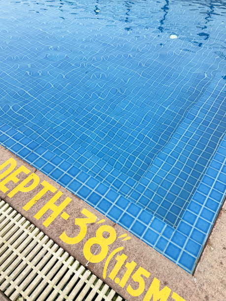 户外泳池台阶的特写图片，游泳池的蓝绿色马赛克瓷砖被荡漾的水扭曲，泳池边的石头露台方板上画着黄色的深度标记警告标志，高架视图图片下载