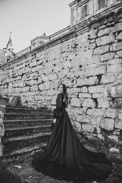 日落时分，身着长裙的女子走在古代宫殿附近的楼梯上。模特女孩走在街上。乌克兰，利沃夫，皮迪西古堡附近的奢侈女子。时尚的新娘。后视图。黑白照片图片下载