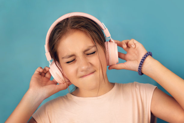 漂亮女孩的照片肖像，闭着眼睛，拿着智能手机听音乐，戴着粉红色的耳机，在蓝色的背景上跳舞图片下载