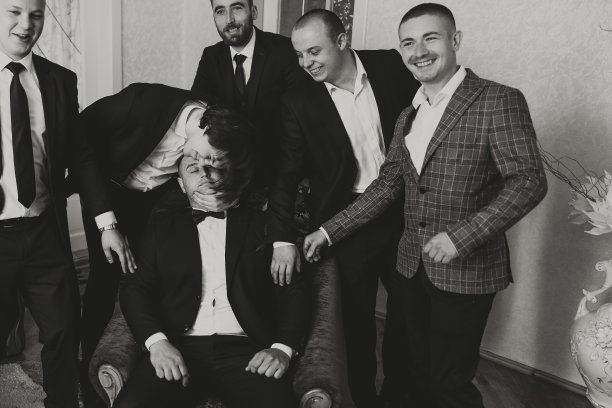 一个年轻的新郎和他有趣的朋友在镜头前摆姿势。一群年轻人拥抱新郎，兴高采烈地向他祝贺。快乐的朋友。房间里有朋友。结婚的那一天。黑白照片。图片下载