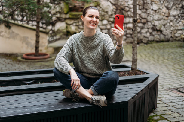 快乐的30岁女人坐在户外的长凳上自拍。年轻漂亮的女孩说你好。都市生活理念，丰满体魄。高质量照片图片下载