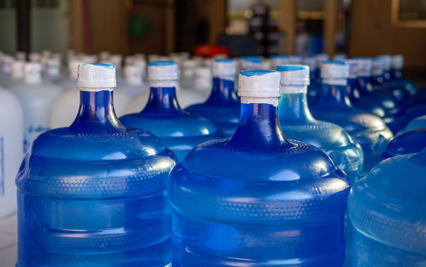 许多蓝色加仑和白色加仑的饮用水排在饮用水生产厂里。图片下载