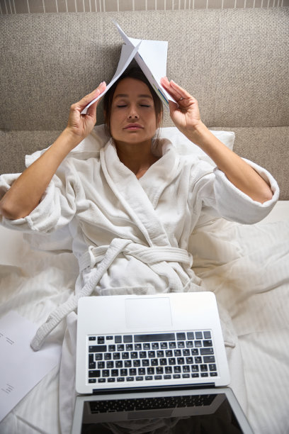 疲惫的女商人用笔记本电脑盖住她的头，在床上放着文件图片下载