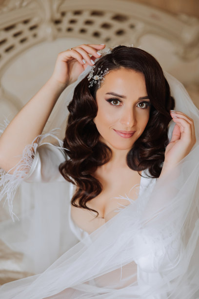 一位漂亮的黑发新娘头戴皇冠，身穿漂亮的睡袍，准备参加婚礼。新娘躺在床上的特写婚纱照，照片。图片下载