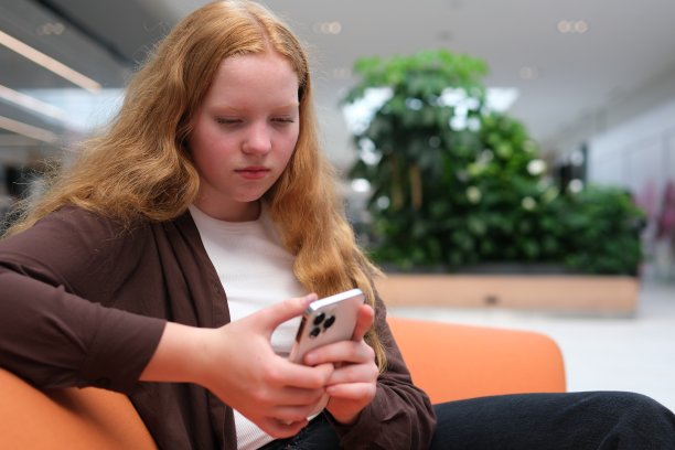 商场里的女孩坐着用手机和朋友交流网上购物，在网上订购，在网上玩游戏，在后台输入文字新闻，人们在商店里走来走去，面目全。图片下载