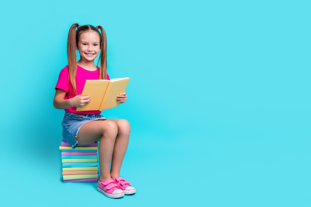 可爱聪明的女学生穿着t恤的全身照片坐在书附近的空白空间做作业孤立的蓝绿色背景图片下载