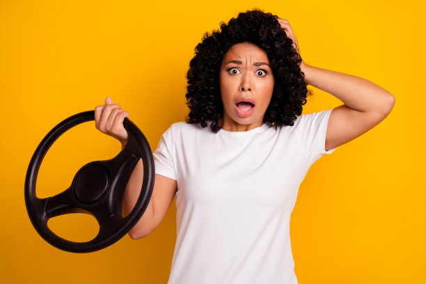 印象深刻的惊恐女士穿着白色t恤，手挽头驾驶汽车孤立的黄色背景的照片图片下载