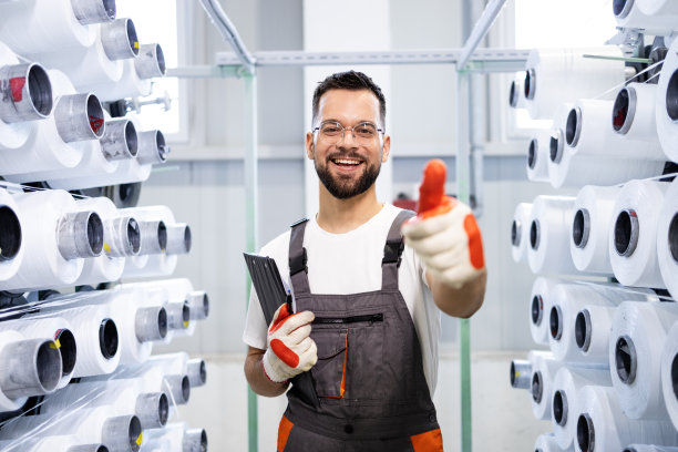 纺织厂工人竖起大拇指，站在工业针织机旁。图片下载