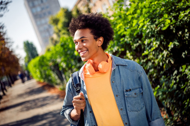 可爱的梦幻男孩戴着牛仔夹克耳机走在城市街道外的大学教育照片图片下载