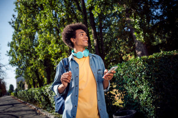 好心情的梦幻男子穿着牛仔夹克，耳机在城市街道外交流现代设备的照片图片下载