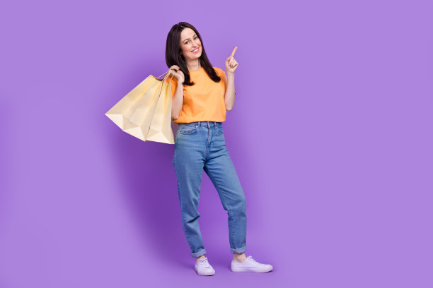 幸福的年轻女子指着空的空间广告牌淘宝店购物孤立的紫色背景的全身照片图片下载
