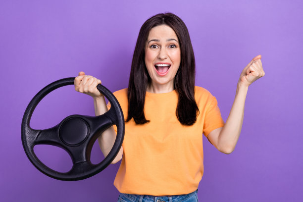 照片中，穿着黄色t恤、喜出望外的年轻有趣女子举起拳头，买下了第一辆汽车，孤立在紫色背景上图片下载