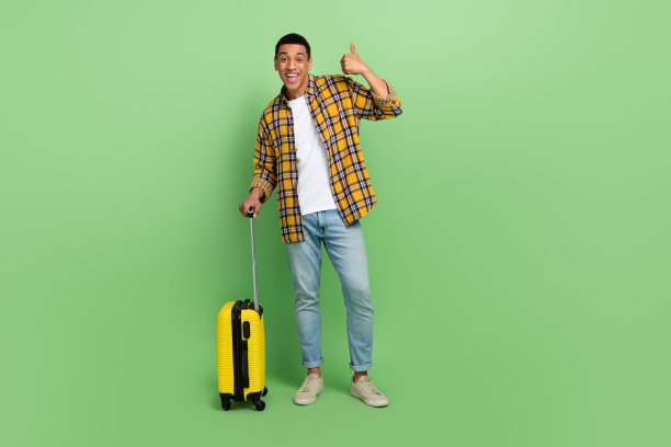 帅哥抱着行李箱的全身照片，在绿色背景上展示拇指向上的空白空间图片下载