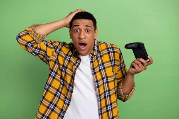 照片中的年轻人穿着格子休闲衬衫，触头盯着电视显示器，震惊地失去了孤立在绿色背景下的比赛图片下载