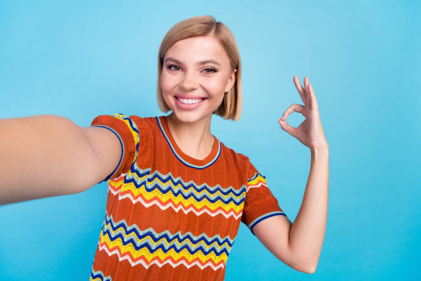 这张照片是一个满意的可爱女人，梳着波波头，穿着针织衫t恤，在蓝色的背景下自拍，显示出孤独图片下载