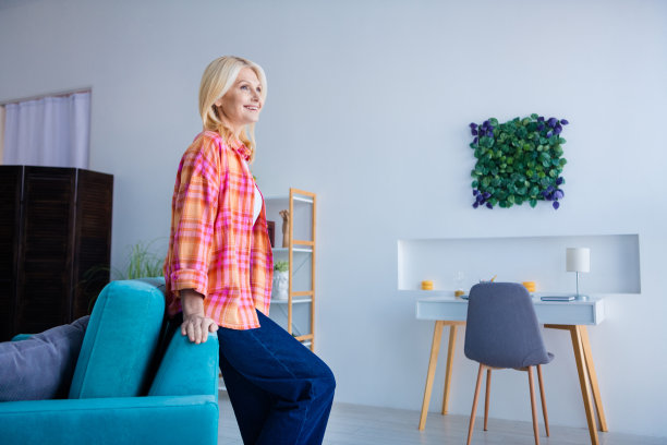 照片上的老积极的高级夫人站在沙发上，看起来梦幻般的新房子公寓室内图片下载
