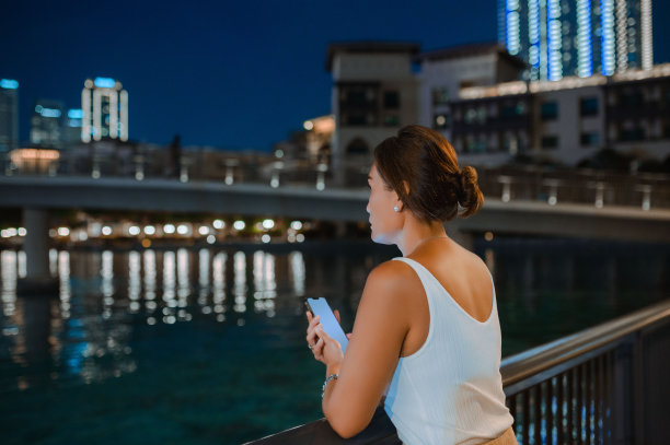 夜晚河边栏杆旁拿手机沉思女人背影图片下载