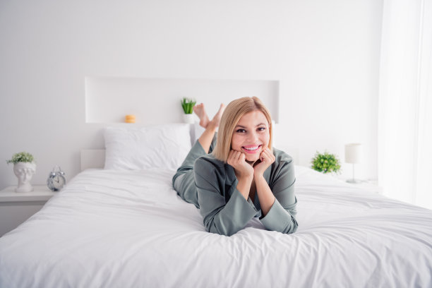 美女的特写照片金发模特穿着品牌睡衣舒适的衣服睡衣睡觉触摸脸颊躺下柔软的白色床图片下载
