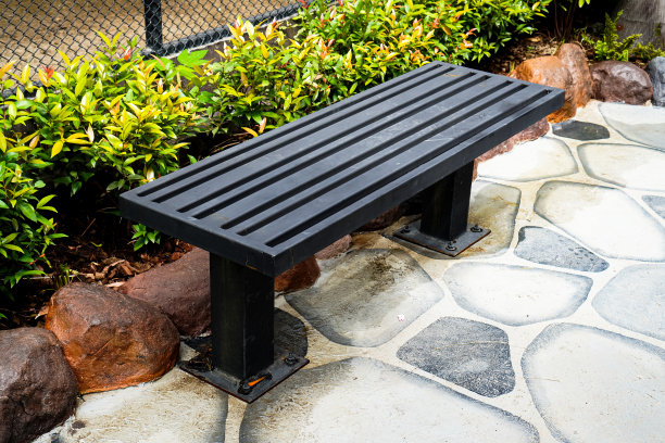 一张黑色金属椅子的图片，它被放置在公共自然公园的人行道上。图片下载