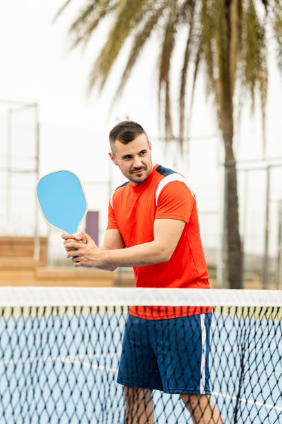一个穿着运动服的成年男子正在打匹克球的垂直照片。这个年轻人在发球时等待接球。泡菜球概念。男子打匹克球。图片下载