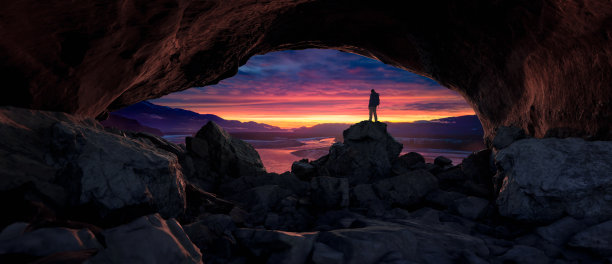 探险人站在岩洞里。背景中的山脉和河流。图片下载