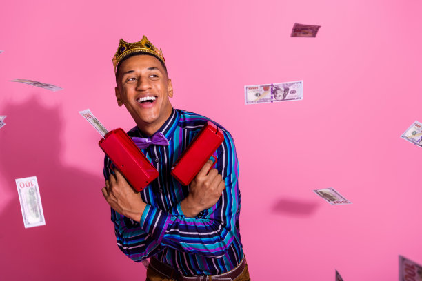 照片时髦开朗的家伙穿条纹衬衫金色皇冠射击钱枪孤立的粉红色背景图片下载