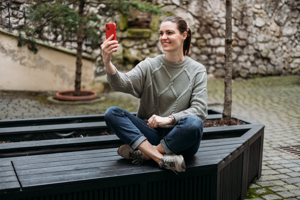快乐的30岁女人坐在户外的长凳上自拍。年轻漂亮的女孩说你好。都市生活理念，丰满体魄。高质量照片图片下载