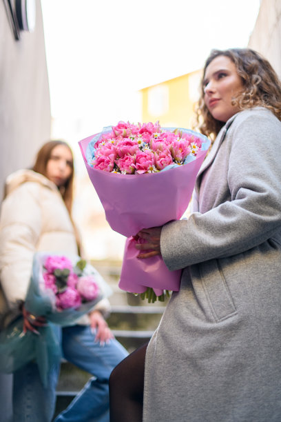 专注于一束美丽的粉红色郁金香和雏菊在一个年轻漂亮的女人的手中图片下载