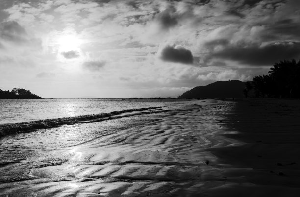 黑暗的海岸景观与湿沙夕阳下的天空。黑白照片图片下载