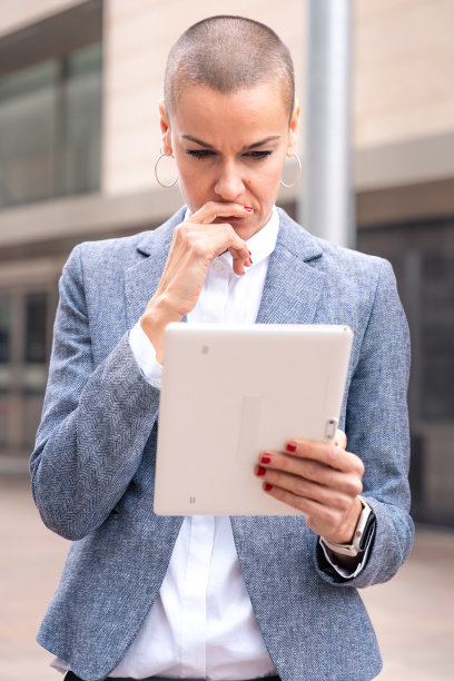 一脸沉思的白人女商人在户外用平板电脑拍摄的垂直照片。图片下载