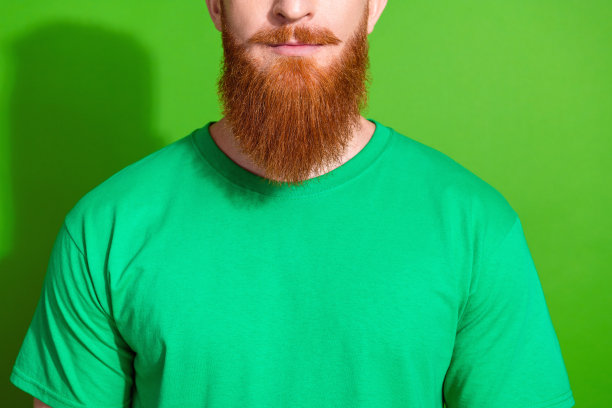 近距离照片帅气的严肃的好心情的男人与姜黄色的长胡子穿着时尚的绿色t恤孤立的绿色背景图片下载