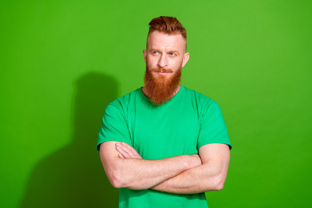 照片中，梦幻体贴的家伙穿着t恤，双臂折叠，看起来空无一物，孤立的绿色背景图片下载