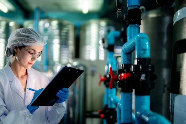 工业工厂的科技工人在检查反渗透机系统的质量。女工在控制面板上记录数据，测量便携式回收装置的压力。图片下载