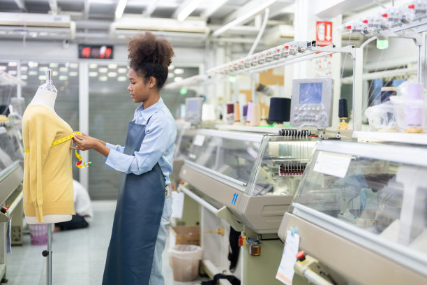 一位美国女设计师认真地按照客户的订单设计服装，并在纺织业中使用大型电脑机器等待出口到国外。图片下载