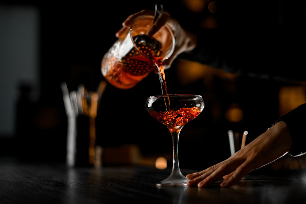 调酒师的手从调酒杯中倒出鸡尾酒，用筛子将其过滤到有柄玻璃杯中图片下载