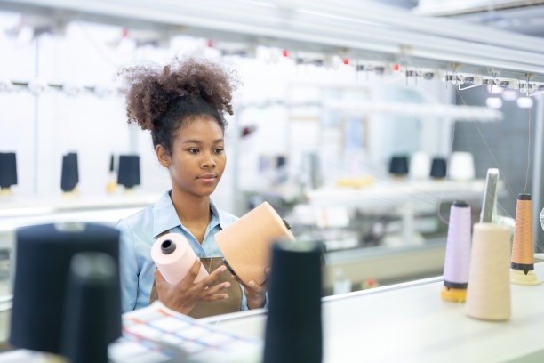 一位美国女设计师拿着一卷卷的彩色线，用来给顾客做衣服，并把它们装进一台大型工业缝纫机，准备出口到世界各地。图片下载