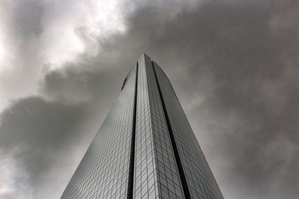 一个令人惊叹的玻璃摩天大楼的低角度视图对着一个戏剧性的多云的天空。图片下载