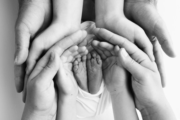 爸爸的手掌，妈妈都抱着刚出生的婴儿的脚。新生儿的脚放在父母的手掌上。工作室微距黑白照片的一个孩子的脚趾，脚跟和脚。图片下载