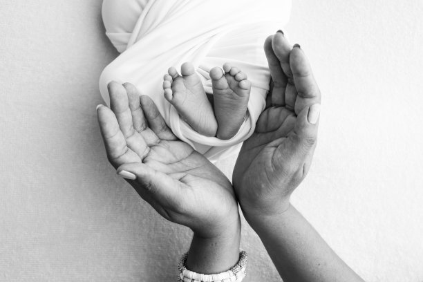 爸爸的手掌，妈妈都抱着刚出生的婴儿的脚。新生儿的脚放在父母的手掌上。工作室微距黑白照片的一个孩子的脚趾，脚跟和脚。图片下载