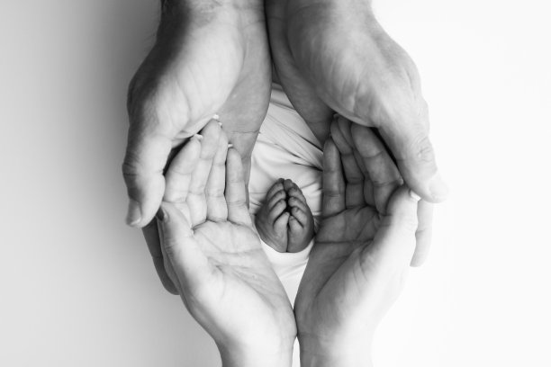 爸爸的手掌，妈妈都抱着刚出生的婴儿的脚。新生儿的脚放在父母的手掌上。工作室微距黑白照片的一个孩子的脚趾，脚跟和脚。图片下载