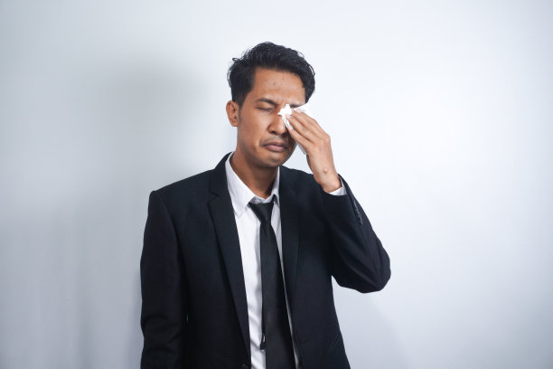 商人擦了擦眼睛。穿着深黑色西装的亚洲年轻经理用白色的纸巾或餐巾擦眼睛。图片下载