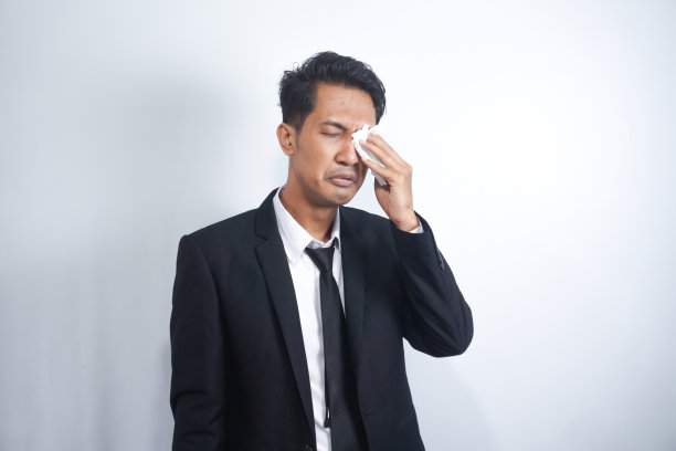 商人擦了擦眼睛。穿着深黑色西装的亚洲年轻经理用白色的纸巾或餐巾擦眼睛。图片下载