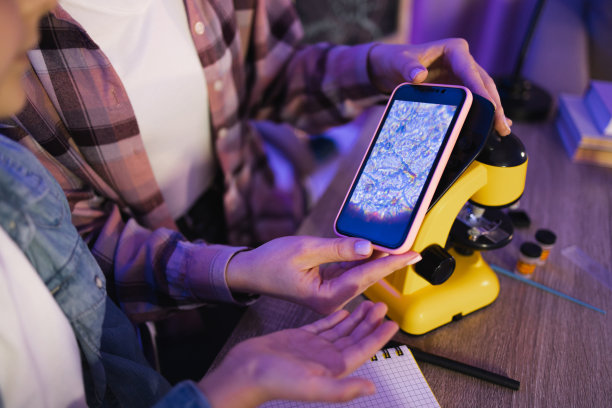 两个女人坐在桌边，在家里用手机做显微照片。图片下载