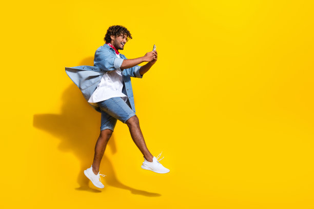 有魅力的年轻人的全身照片跑步手持设备穿着时尚的牛仔服装红色围巾孤立的黄色背景图片下载